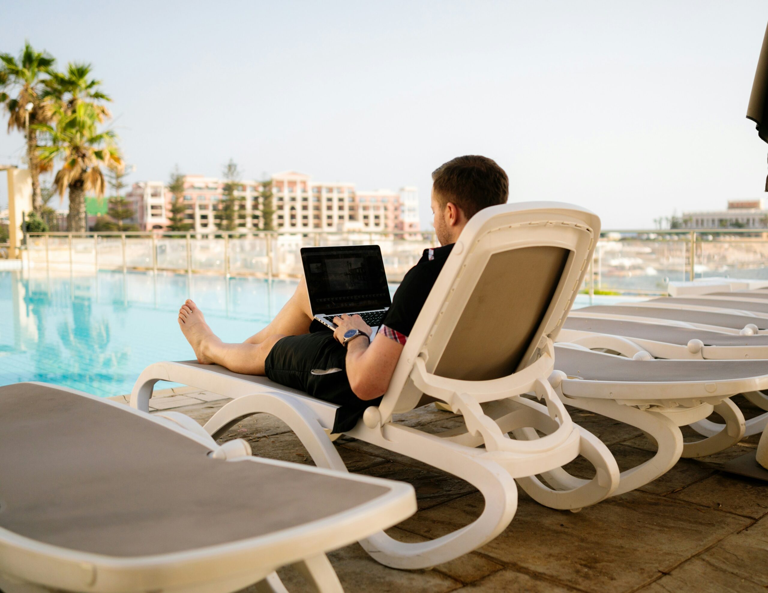 man on laptop lounging next to pool